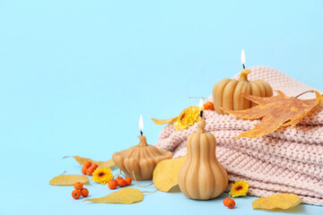 Beautiful composition with burning candles in shape of pumpkin, plaid and autumn leaves on blue background