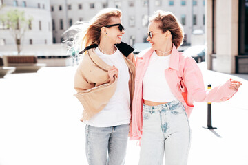 Two young beautiful smiling hipster female in trendy summer clothes. Carefree women posing in the street. Positive models having fun outdoors at sunny day. Cheerful and happy. In sunglasses