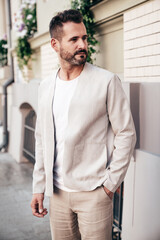 Portrait of handsome confident stylish hipster lambersexual model. Sexy modern man dressed in elegant suit. Fashion male posing in the street background in Europe city at sunset. In sunglasses