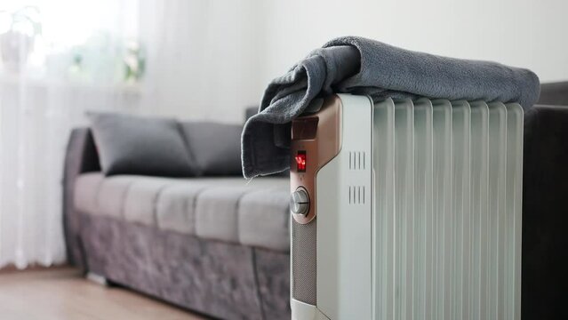 A man folds a blanket from the sofa and places it on an electric heater. Fire and fire hazard concept. Copy space for text