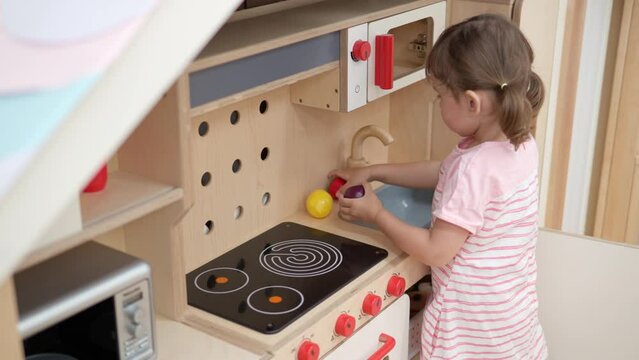 Little Girl Playing in Toy Kitchen Washing Fruits in Sink