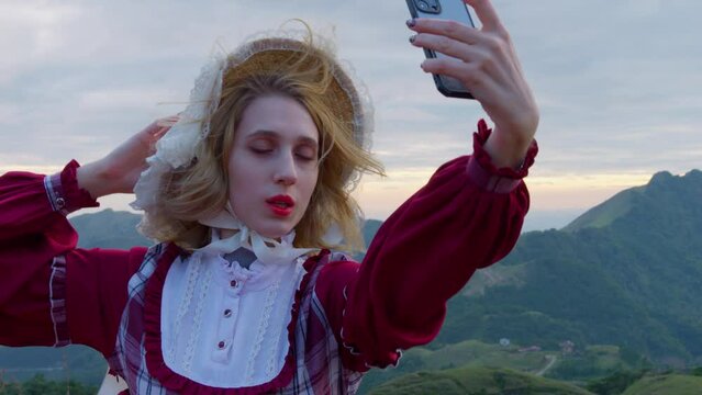 Woman poses to take selfie at top of mountain overlook wearing european mountain village dress