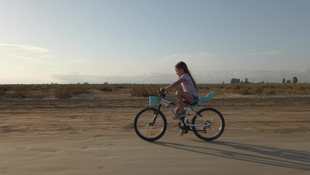 Little girl riding a bicycle on a sandy road as the sun shines at dusk