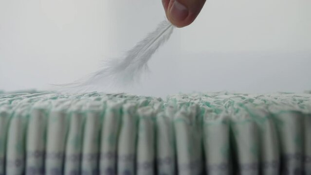 A feather runs over a stack of baby diapers on a white background. The concept of softness and comfort, children's hygiene. Copy space for text