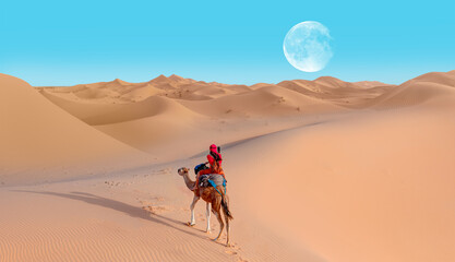 A woman in a red turban riding a camel across the thin sand dunes of the in Western Sahara Desert, Morocco, Africa "Elements of this image furnished by NASA"