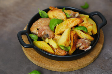 Fried chicken and potatoes in the black plate on wooden plate, brown background, top view.