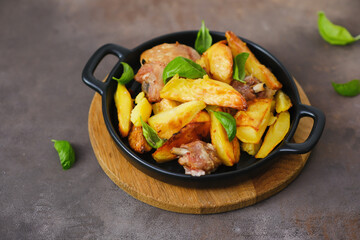 Fried chicken and potatoes in the black plate on wooden plate, brown background, top view.