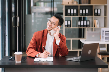 Young handsome man typing on tablet and laptop while sitting at the working wooden table modern office.