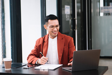 Obraz premium Young handsome man typing on tablet and laptop while sitting at the working wooden table modern office.