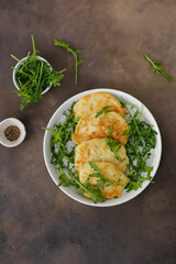 Zucchini pancakes with arugula in a white plate on a brown background. Top view.