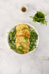 Zucchini pancakes with arugula in a white plate on a marble background. Top view.