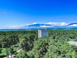 a lonely high-rise building standing in a green forest thicket against the backdrop of mountains...