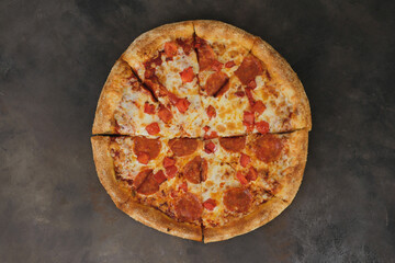 Slices of fresh round pizza with saucages, cheese on dark brown background, top view.