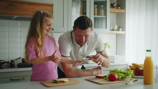 The smiling loving father and daughter standing in the kitchen at the table, he helps cooking sandwiches, hugs and kisses her. Showing a high five gesture for a job well done. The concept of happy