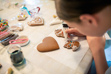 Close-up of a young girl decorating gingerbread cookies with icing. - 661344103
