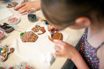 Close-up of a young girl decorating gingerbread cookies with icing. - 661344142