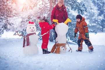 Family building a cute snowman in the snowy park.