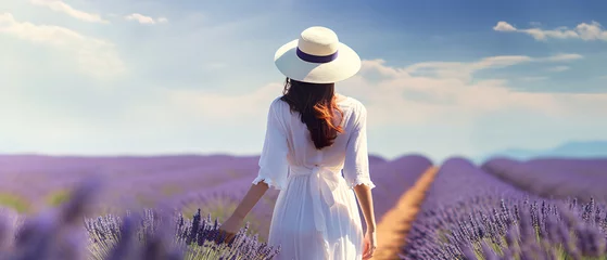 Rolgordijnen Rear view of a young woman in a white dress and hat walking through a purple lavender field. natural background concept © Ton Photographer4289