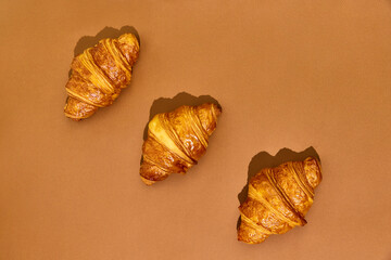 Three crispy freshly baked croissants isolated over brown background. Yummy taste, salted and sweet. Concept of food, bakery, breakfast ideas, taste, freshness. Poser. Copy space for ad