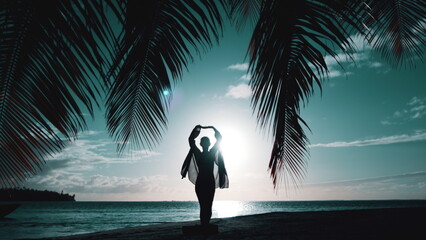 Woman walking on night tropical beach. Silhouette of slim girl under the palm coconut tree raise...