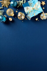 Christmas poster, party invitation card template. Flat lay glistening gold and blue balls, gift box with ribbon bow, fir branches on dark blue background. Top view. Flat lay.