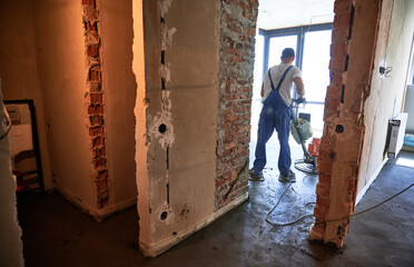 Worker using troweling machine while screeding floor in apartment under renovation. Man finishing...