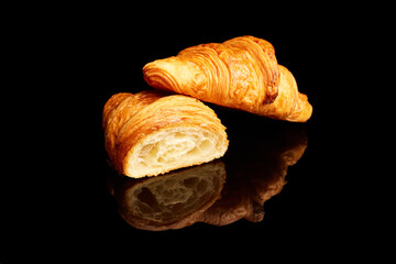 Crispy, fresh croissant, whole and cut in half isolated over black background with reflection. Concept of food, bakery, breakfast ideas, taste, freshness. Poser. Copy space for ad