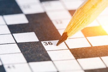 Simple pencil on background of closeup crossword puzzle with bright illumination.