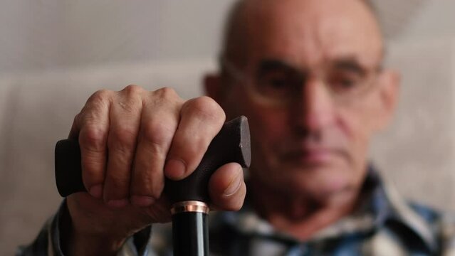 Close up side profile photo of grey hair he his him grandpa leaning with grief on walking stick looking straight oldness in mind casual checkered shirt sitting on cozy divan