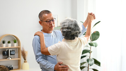 Affectionate senior couple dancing in living room, enjoying retired life and spending free time...