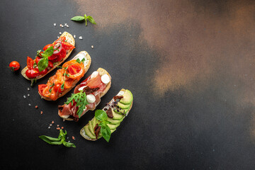 a set of bruschetta with prosciutto, salmon, tomatoes and avocado on a dark background. top view. place for text