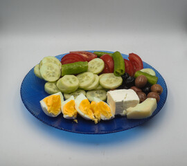 Eggs, cucumbers, tomatoes, olives, olives, chillies and cheese in a blue glass breakfast plate on a...
