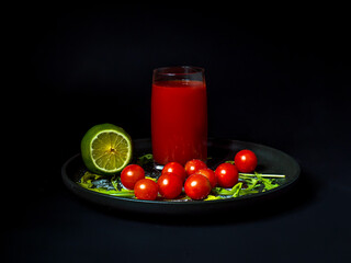 A glass of tomato juice on a black plate with cherry tomatoes and lime