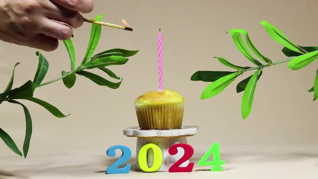 happy new year 2024 concept, hand lighting a candle birthday cupcake decorated with ruscus plants