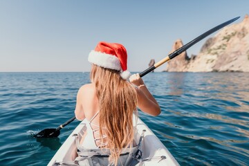 Woman in kayak back view. Happy young woman in Santa hat floating in kayak on calm sea. Summer...