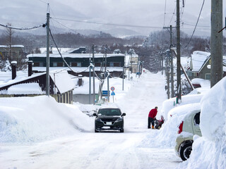 Car driving in a heavy snowfall area with a person handling a snowblower (Niseko, Hokkaido, Japan)