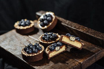 Obraz na płótnie Canvas Chocolate tartlets decorated with blueberries on a dark wooden background. Beautiful portion cakes for the holiday table. Dessert with fresh blueberries.