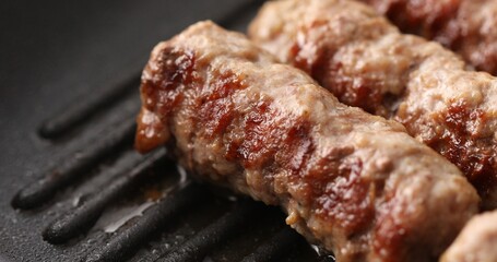 Minced meat sausages are fryed on a grill pan with steam or smoke. Close-up dolly shot. Frying traditional Balkan chevapi. Cooking food.