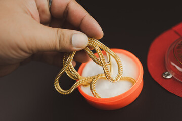Man hand pick up of Gold necklace in a orange box. Designer thick gold curb for men