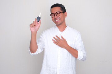 Adult Asian man smiling happy while looking to a car key that he hold - obrazy, fototapety, plakaty