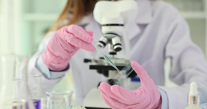 Scientist holds pipette and drops sample of blue solution onto glass plate for microscope. Research and experiment with vaccine and work in laboratory