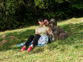 Happy family mother with daughter and two dogs sitting on green grass lawn having fun picnic spending time together hiking in the mountains. People and pets outdoors lifestyle photo candid emotions.