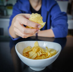 Woman using her hand to pick up potato chips from a bowl, closed up shot.