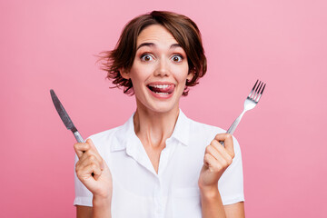 Photo of pretty charming toothy girl licks her teeth she is hungry waiting eating using fork and knife isolated on pink color background