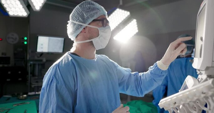 Doctors, digital machine or heart monitor in theater, hospital or operation room for surgery or cardiology. Surgeon, medical or professional click or press ecg screen for cardiovascular check and ppe