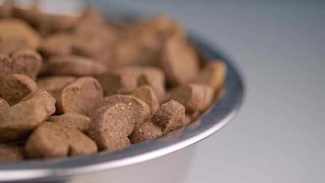 Canine dry food, resembling hearts, turns leisurely in a bowl. Light background emphasizes pet-owner bond.