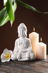 Buddha statue, flower, candles and bamboo on brown background