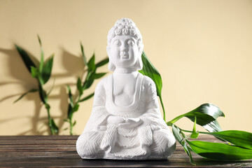 Buddha statue and bamboo on wooden table on beige background