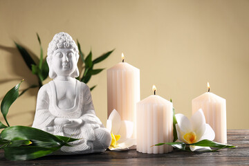Buddha statue, bamboo, candles and flowers on beige background