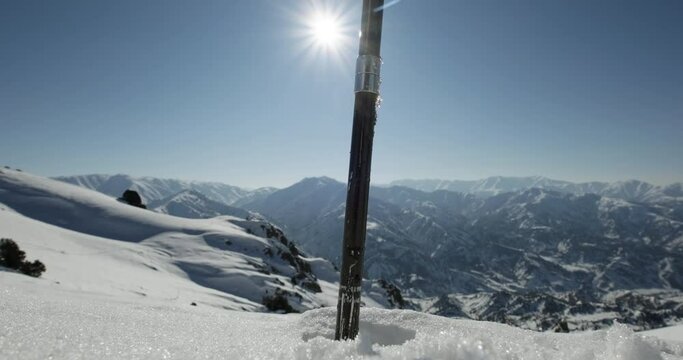 Ski pole sticks into mountain snow. Skier tourist climbs slope. Epic mountain view, sunny clear day. Snowflakes glisten in sun as ski pole pulled out of snowdrift. Hiking climbing mountain. Close up